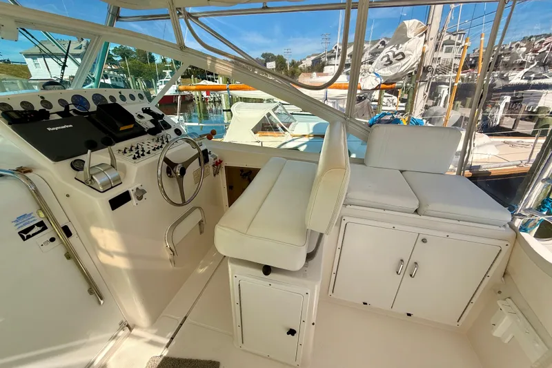 Slide: The Image of 2001 Cabo 35 Express boat helm with white seating and control panel, docked at marina. - 34