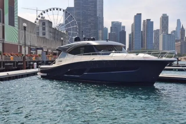 The Image of 2025 Riviera 585 SUV yacht docked in urban marina with city skyline backdrop. - 0