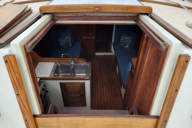 Slide: The Image of Interior view of a 1976 Down East Yachts Cutter, featuring a compact kitchen and cozy seating area. - 10