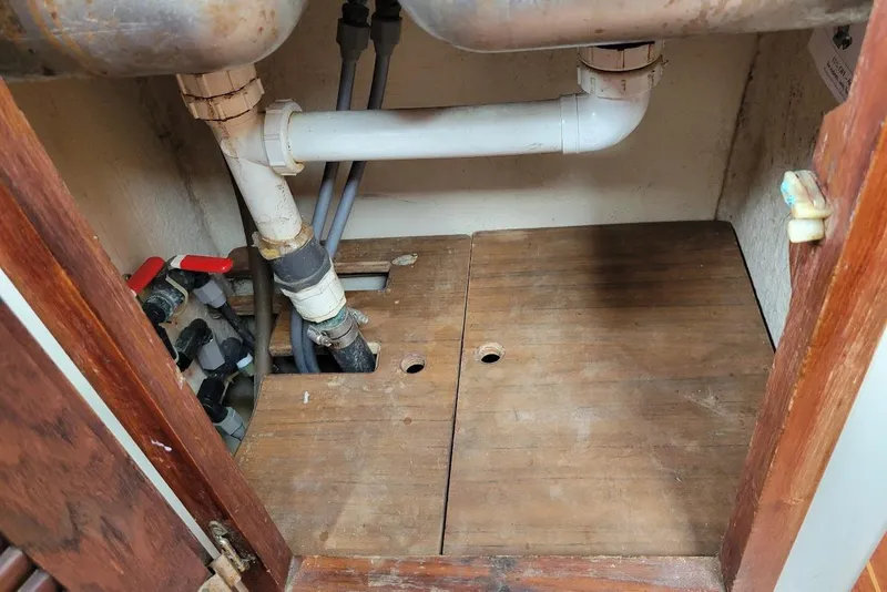 Slide: The Image of Under-sink plumbing in a 1976 Down East Yachts Cutter, featuring pipes and wooden cabinetry. - 14