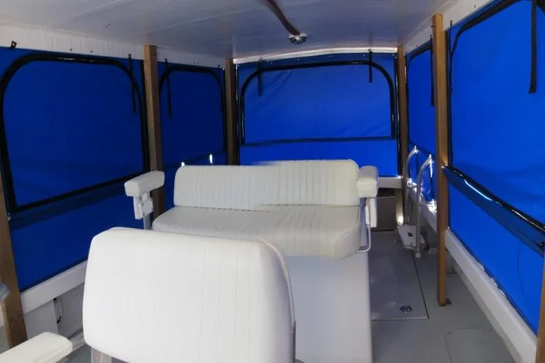 Slide: The Image of 2010 Ellis Downeast Picnic Boat interior with white seating, blue covers, docked at marina. - 2