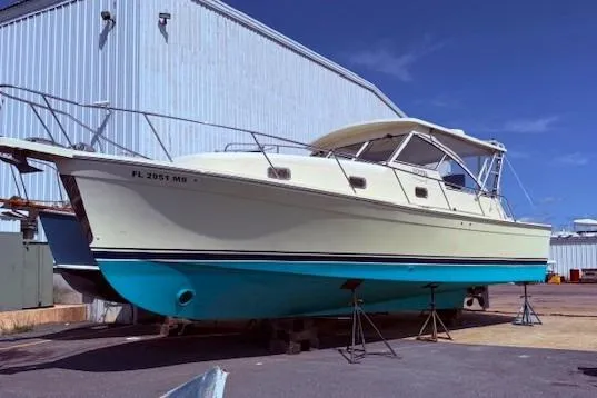 Slide: The Image of 2004 Mainship Pilot 34 boat on stands, cream hull, blue bottom, near industrial building. - 1
