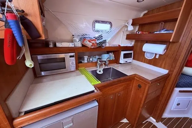 Slide: The Image of 2004 Mainship Pilot 34 galley with wooden cabinetry, sink, microwave, and storage shelves. - 14