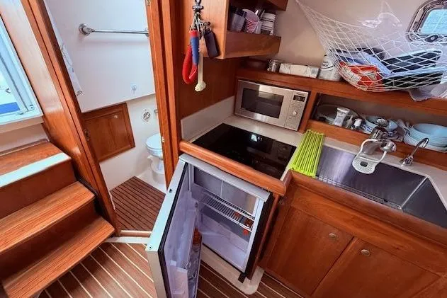 Slide: The Image of 2004 Mainship Pilot 34 galley with fridge, microwave, sink, and wooden cabinetry. - 15