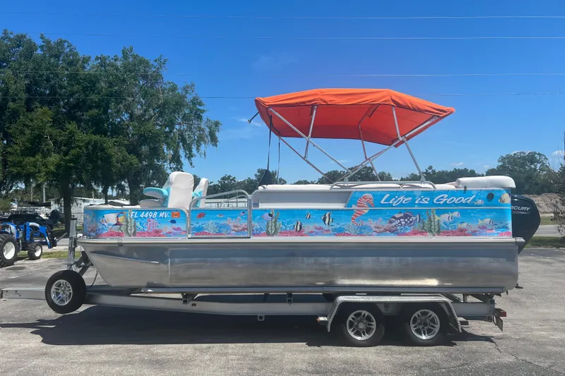 Slide: The Image of 2005 G3 LX20 pontoon boat with vibrant marine graphics and orange canopy on trailer. - 5