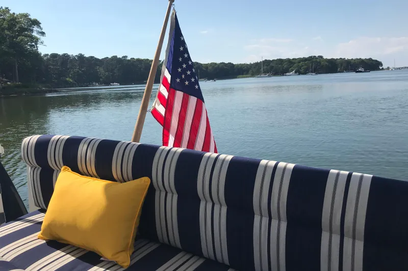 Slide: The Image of 2008 Back Cove 33 Hard Top Express with striped seating, yellow pillow, and American flag on calm water. - 5