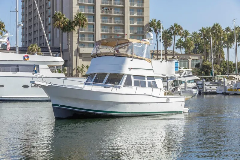Slide: The Image of 2001 Mainship 390 Trawler docked in marina, surrounded by palm trees and buildings. - 0
