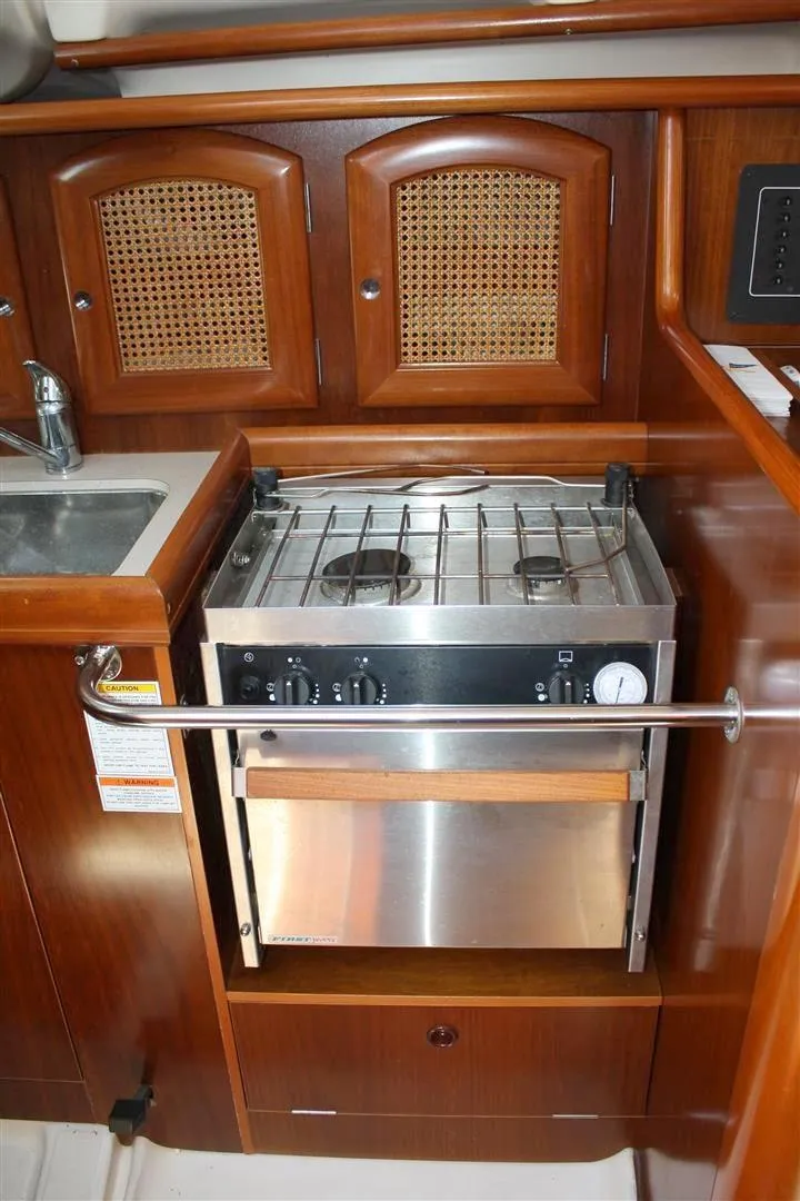 Slide: The Image of 1999 Beneteau Oceanis 352 yacht kitchen with stove and wooden cabinetry. - 24