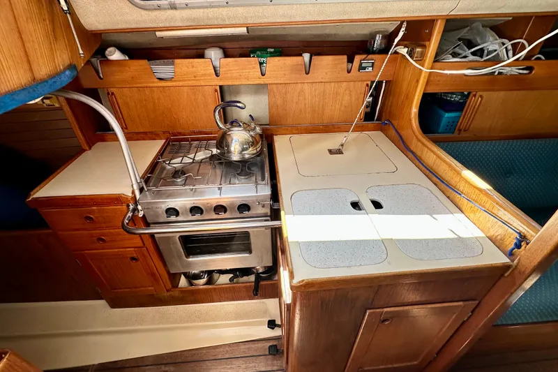 Slide: The Image of Compact kitchen in a 1983 Sirena 38 sailboat with stove, sink, and wooden cabinetry. - 3