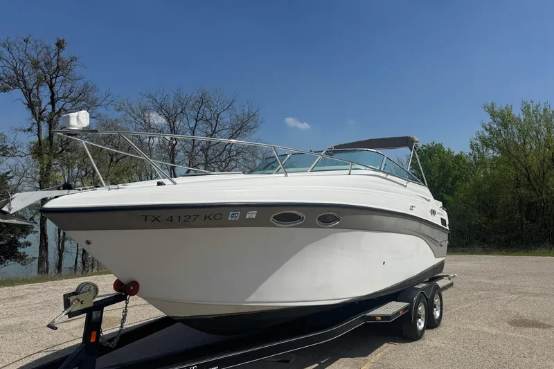 Slide: The Image of 2003 Crownline 262 CR boat on trailer, parked near trees under clear blue sky. - 11