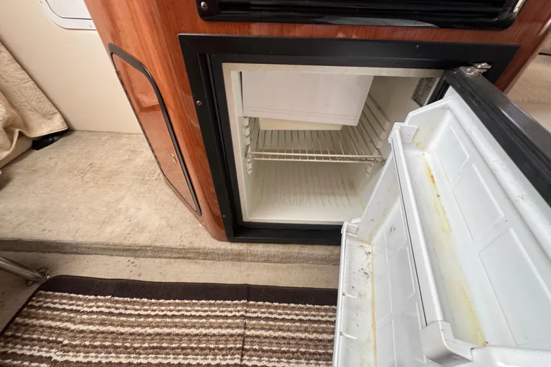 Slide: The Image of Open mini fridge inside 2003 Crownline 262 CR boat cabin, showing interior shelves. - 17