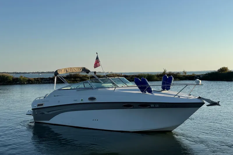Slide: The Image of 2003 Crownline 262 CR boat on calm water with American flag. - 2
