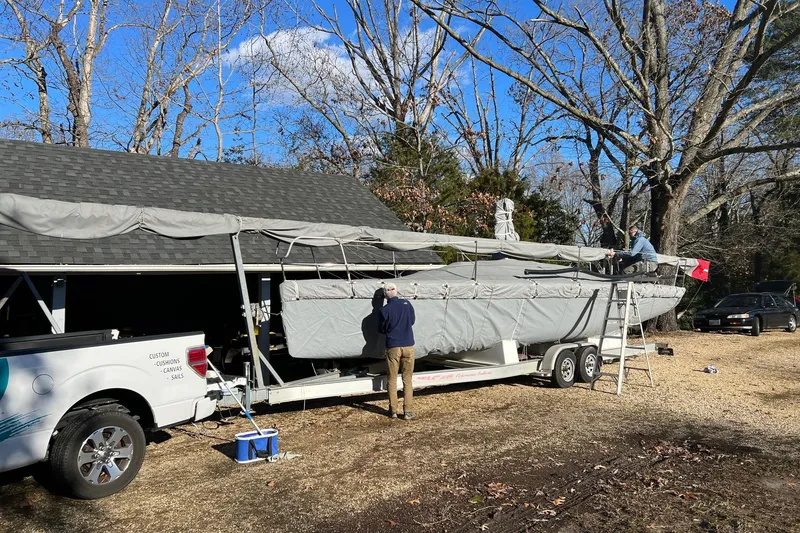 Slide: The Image of 2010 Melges 32 sailboat on trailer, covered, with people working nearby, surrounded by trees. - 2