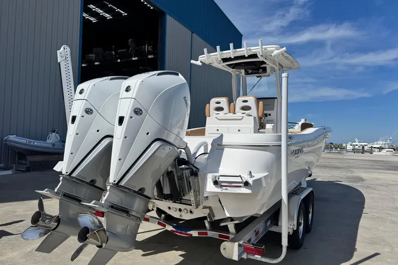 Slide: The Image of 2026 Caymas 291 boat with dual outboard motors on a trailer, dockside view. - 6