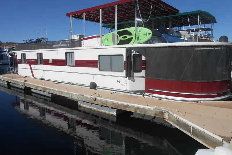 The Image of 1988 Lazy Days houseboat docked, featuring red accents and rooftop kayaks. - 0