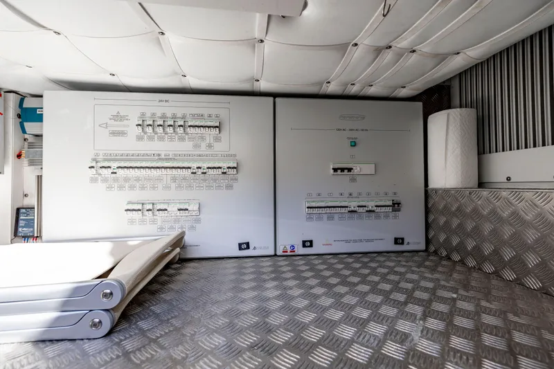 Slide: The Image of Electrical control panels inside a 2021 Pershing 62 yacht, featuring circuit breakers and metallic flooring. - 131