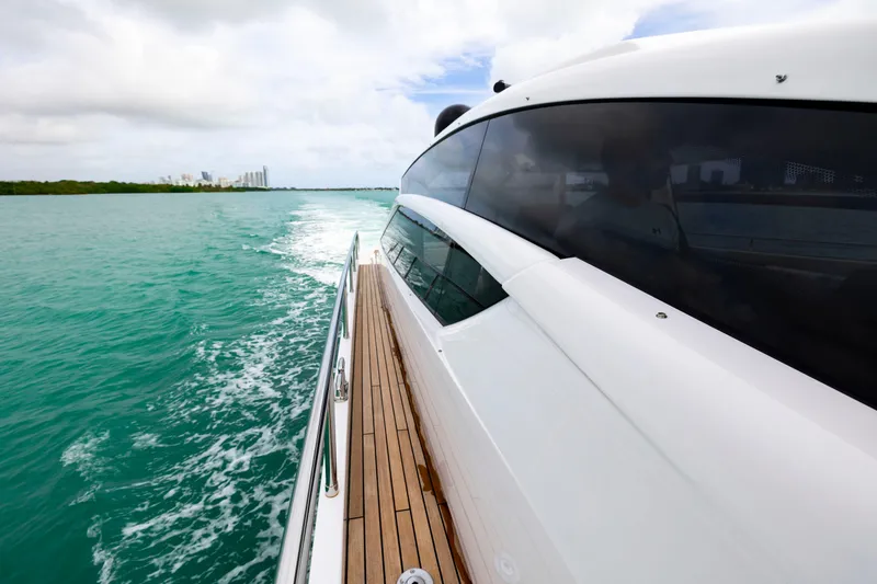 Slide: The Image of 2021 Pershing 62 yacht cruising on turquoise waters, showcasing sleek design and wooden deck. - 32
