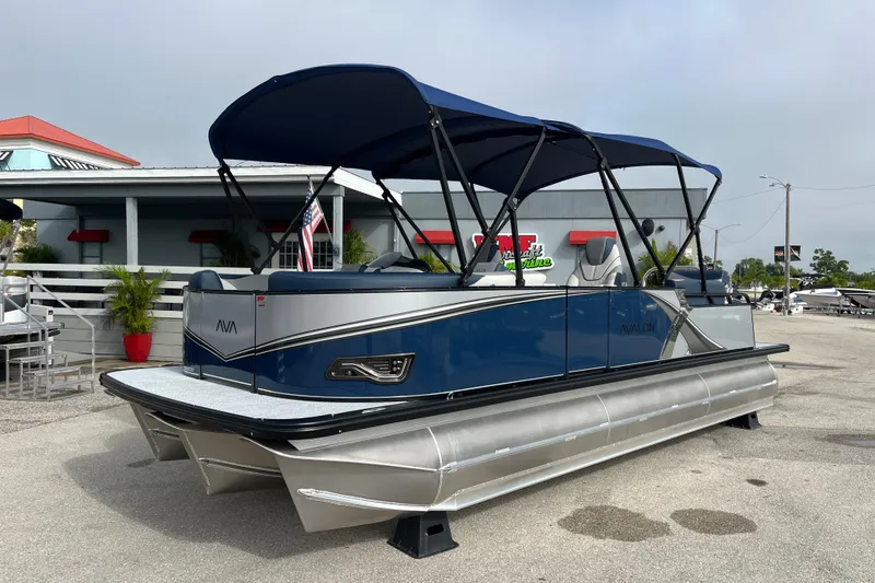 The Image of 2026 Avalon 2385 LSZ Quad Lounger Tri Toon boat with blue canopy in marina setting. - 1