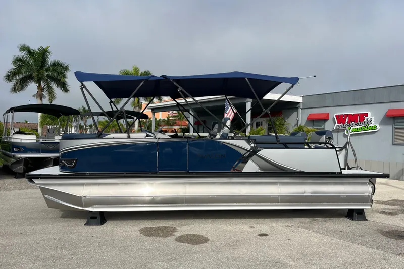 Slide: The Image of 2026 Avalon 2385 LSZ Quad Lounger Tri Toon boat with blue canopy, parked outdoors. - 8