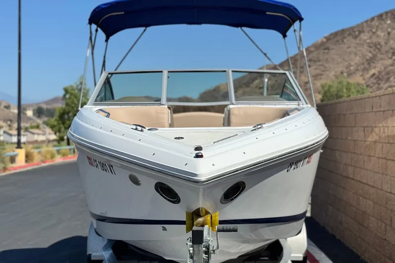 Slide: The Image of 2008 Cobalt 262 boat with blue canopy, parked on a trailer, mountain background. - 2