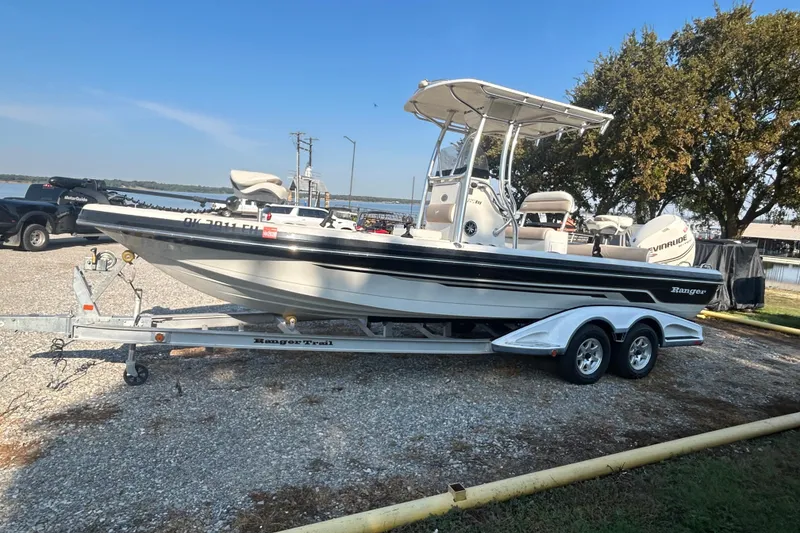Slide: The Image of 2009 Ranger 2410 Bay Ranger boat on trailer, parked near a lake under clear skies. - 2