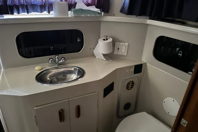 Slide: The Image of 1990 Carver 3608 Aft Cabin bathroom with sink, toilet, and porthole windows. - 16