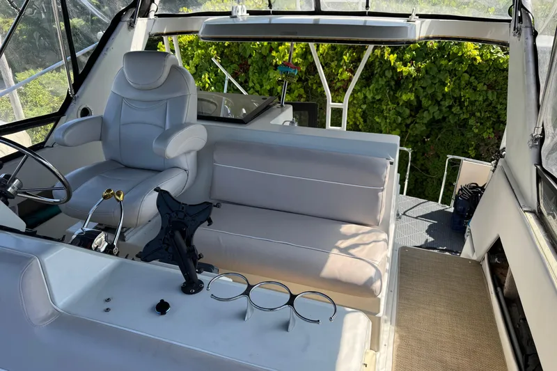 Slide: The Image of 1990 Carver 3608 Aft Cabin interior with helm, seating, and lush greenery outside. - 21