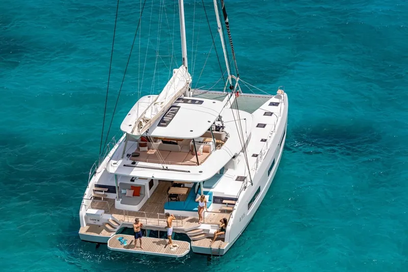 Slide: The Image of 2026 Lagoon 55 catamaran sailing on clear turquoise waters, with people enjoying the deck. - 11