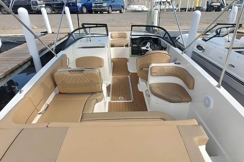 Slide: The Image of 2025 Bayliner VR6 Bowrider OB interior with tan seating and wood accents at a marina. - 7