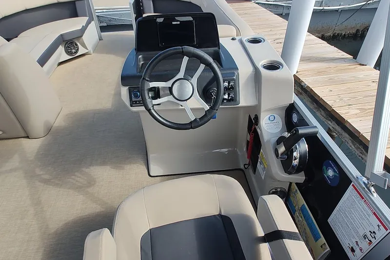 Slide: The Image of 2024 Harris Cruiser 230 boat interior with steering wheel and seating, docked by wooden pier. - 5