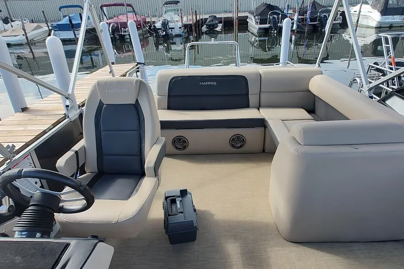 Slide: The Image of 2024 Harris Cruiser 230 boat interior with plush seating and steering wheel, docked at marina. - 6
