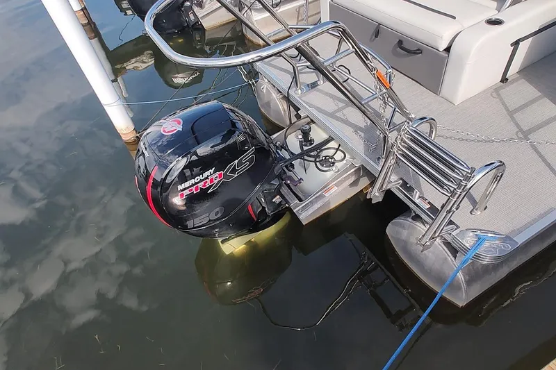 Slide: The Image of 2024 Crest Classic LX 220 pontoon boat with Mercury 150 engine, docked on calm water. - 11