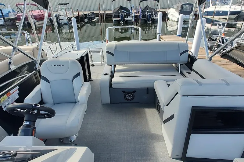 Slide: The Image of 2023 Crest Classic LX 220 boat interior with plush seating and steering wheel, docked at marina. - 3