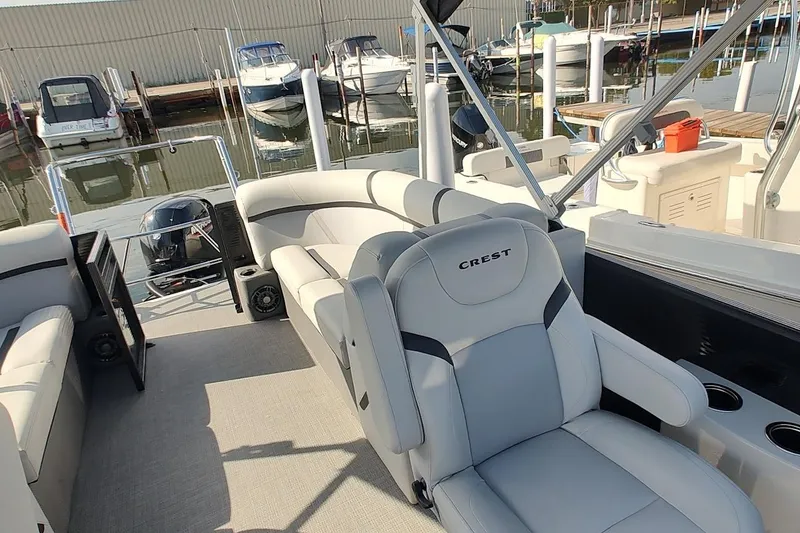 Slide: The Image of 2024 Crest Classic LX 220 pontoon boat interior with plush seating at marina. - 6