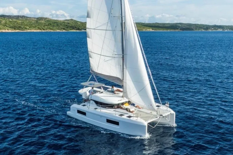 Slide: The Image of 2026 Lagoon 38 catamaran sailing on open blue sea near a lush coastline. - 2