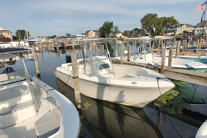 Slide: The Image of 2023 Cobia 237 Center Console boat docked in a marina with surrounding boats. - 2
