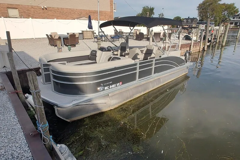 The Image of 2024 Harris Cruiser 230 pontoon boat docked by a waterfront patio. - 0