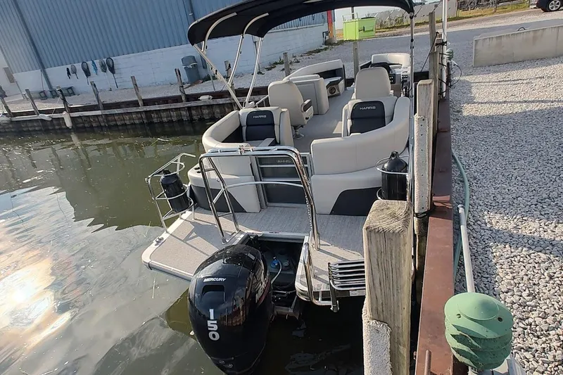 Slide: The Image of 2024 Harris Cruiser 230 pontoon boat docked, featuring spacious seating and a Mercury 150 engine. - 4