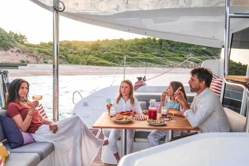 Slide: The Image of Family enjoying a meal on a 2026 Lagoon 38 yacht, anchored near a scenic beach. - 6