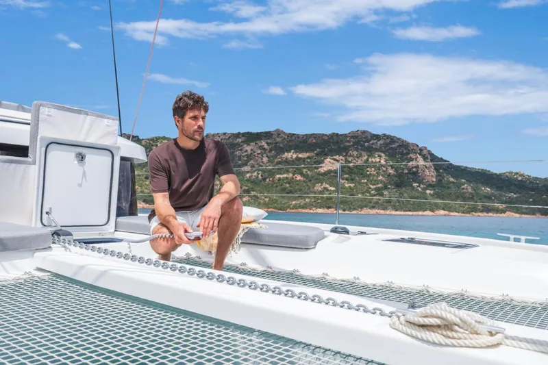 Slide: The Image of Man relaxing on Lagoon 38 catamaran, 2026 model, with scenic coastal backdrop. - 7