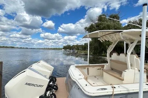 Slide: The Image of 2019 Scout 355 LXF boat docked by a scenic lake under a cloudy sky. - 12
