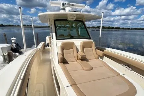 Slide: The Image of 2019 Scout 355 LXF boat with tan seating, docked by a scenic lake. - 17