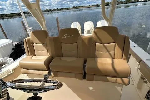 Slide: The Image of 2019 Scout 355 LXF boat with tan leather seating and steering wheel, docked by a lake. - 28