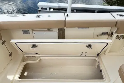 Slide: The Image of 2019 Scout 355 LXF boat with open storage compartment, beige seating, and water in the background. - 48