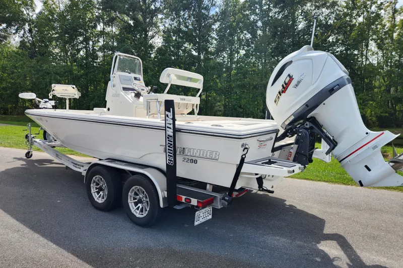 Slide: The Image of 2024 Pathfinder 2200 TRS boat on trailer with powerful outboard motor, parked outdoors. - 2