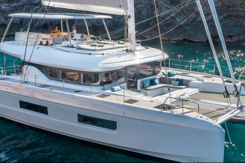 The Image of 2026 Lagoon 60 yacht sailing in clear blue waters near rocky coastline. - 0