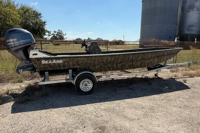 The Image of 2025 SeaArk 1860 MVJT boat on trailer, camo design, parked outdoors. - 0