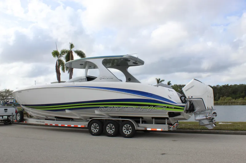 Slide: The Image of 2020 Mystic Powerboats M4200 on trailer by a lake, featuring sleek design and vibrant graphics. - 4
