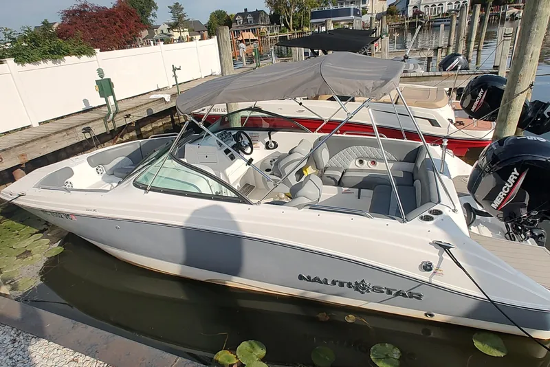 Slide: The Image of 2026 NauticStar 223 DC Deck boat docked, featuring a sleek design and spacious seating. - 3