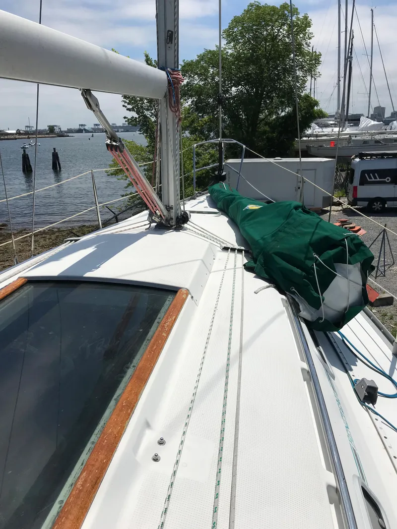 Slide: The Image of 1993 Beneteau First 310 sailboat deck with green sail cover, docked by the water. - 11